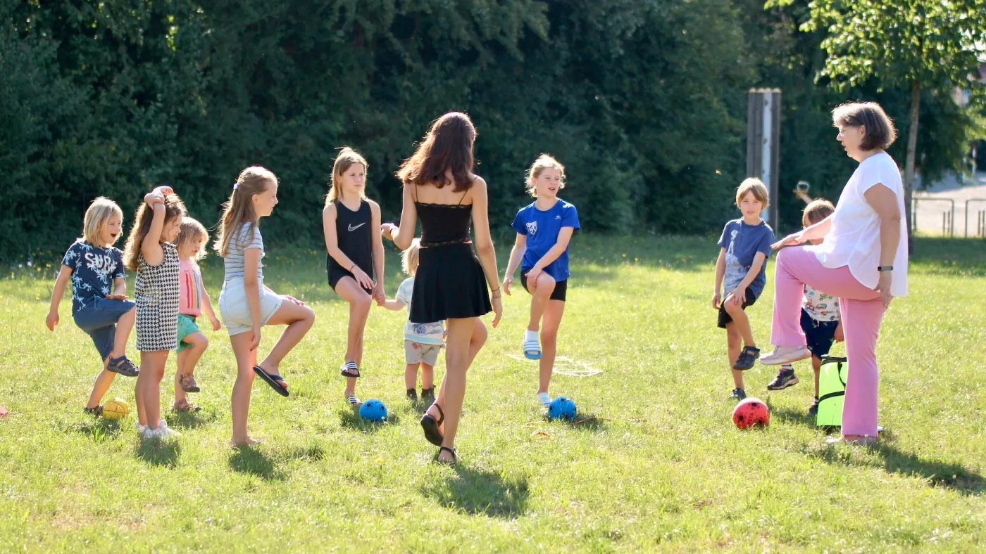 Kindergruppe bei einer Bewegungsübung auf einer Wiese, angeleitet von Jutta Gelbke